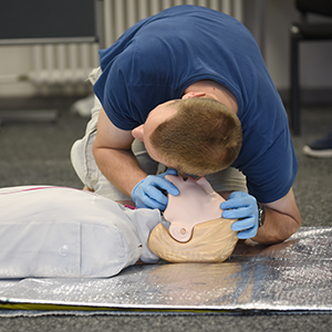 Teilnehmer einer Erste-Hilfe-Breitenausbildung des Deutschen Roten Kreuzes führt Beatmung an einer Trainingspuppe auf einer Rettungsdecke durch.